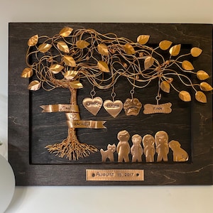May include: A copper wire family tree art piece with a brown wooden frame. The tree has gold leaves and copper wire branches. The names John, Rachel, Chris, Alyna, Luna, and Finn are written on the tree. The date August 15, 2017 is written on the bottom of the frame.