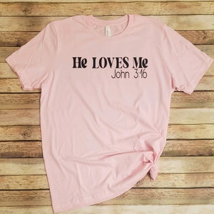 May include: Pink t-shirt with black text that reads "He LOVES Me John 3:16".