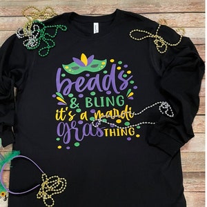 May include: Black long-sleeve shirt with a purple and green design that says "beads & bling it's a mardi gras thing".