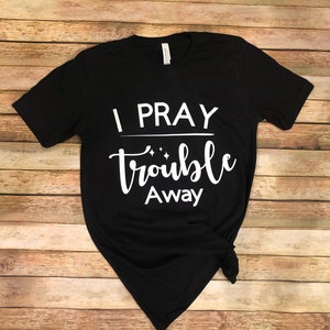 May include: Black t-shirt with white text that reads "I pray trouble away".