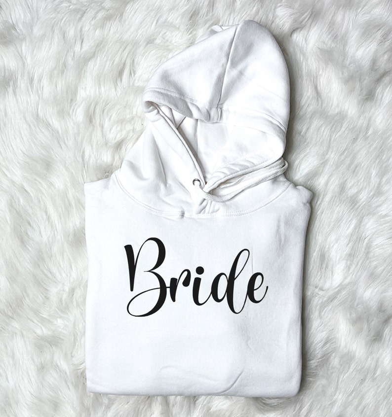 以下が含まれることがあります： 白いフード付きスウェットシャツに、黒い筆記体で「Bride」とプリントされています。