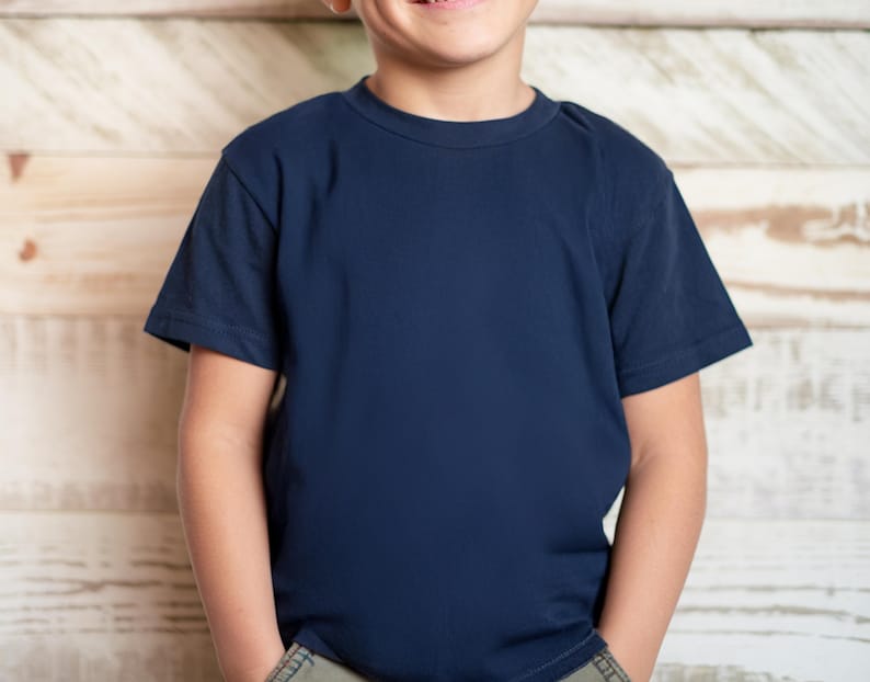May include: A navy blue crew neck t-shirt. The short-sleeved shirt is made of a soft material. The shirt is shown on a person in front of a light brown wooden background.