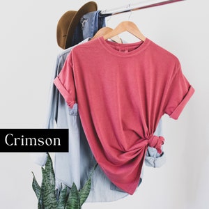 Pode incluir: Camiseta de cor carmesim com mangas dobradas pendurada em um cabide de madeira.