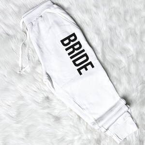 以下が含まれることがあります： 脚に黒で「BRIDE」とプリントされた白いスウェットパンツです。