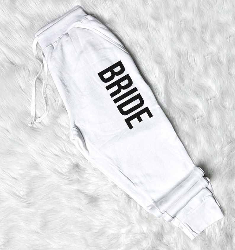 以下が含まれることがあります： 脚に黒で「BRIDE」とプリントされた白いスウェットパンツです。