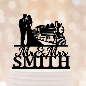 Op de afbeelding: Een zwart silhouet van een stel dat voor een trein staat met de tekst "Mr. & Mrs. SMITH" op een witte bruidstaart versierd met witte bloemen.