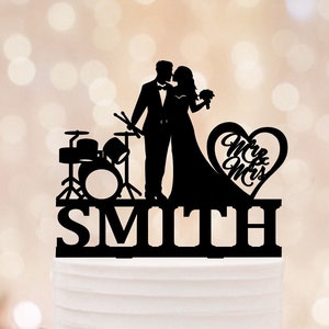Può includere: Silhouette nera di una sposa e uno sposo con una batteria e il testo "Mr. & Mrs. Smith" su una torta nuziale bianca.