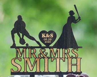 Può includere: Un topper per torta nuziale in legno con una silhouette di coppia a tema baseball. Lo sposo è in posizione di battuta, mentre la sposa tiene una mazza. Il topper include il testo "MR & MRS SMITH" e un cuore con le iniziali "K&S" e la data "08.29.2020".