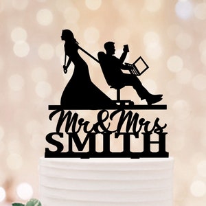 Könnte beinhalten: Schwarzer Silhouetten-Kuchentopper einer Braut, die einen Bräutigam zieht, der auf einem Stuhl mit einem Laptop sitzt. Der Text "Mr. & Mrs. Smith" befindet sich unter den Figuren.