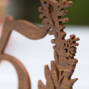 May include: A wooden table number with the number "5" carved into it. The number is surrounded by a decorative floral design.
