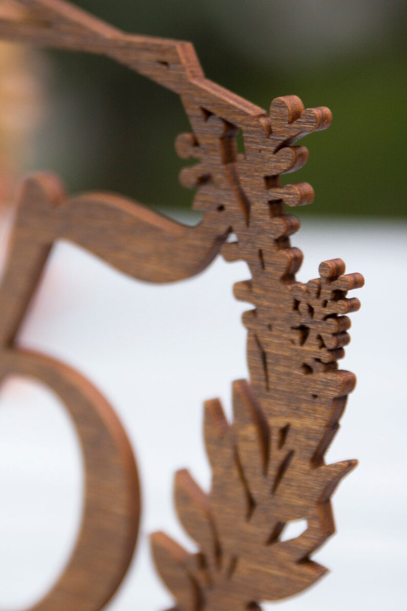 May include: A wooden table number with the number "5" carved into it. The number is surrounded by a decorative floral design.