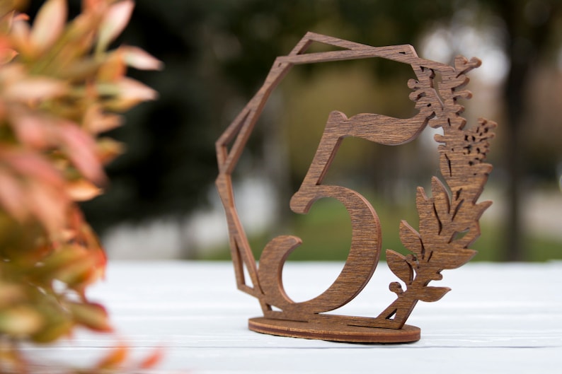 May include: Wooden table number with the number 5 cut out in the center. The number is surrounded by a geometric design and a floral design.