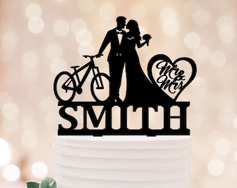 May include: Black silhouette of a couple kissing, with a bicycle behind them, a heart with the text "Mr & Mrs" and the last name "Smith" below. This is a wedding cake topper.