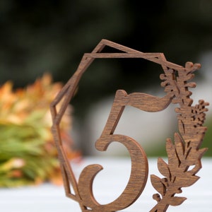 May include: Wooden table number with the number 5 cut out in the center. The number is surrounded by a decorative floral design.