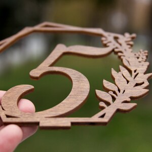 May include: A wooden table number with the number "5" cut out in the center. The number is surrounded by a decorative floral design.