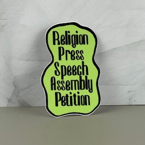 May include: A sticker with a lime green background and a black outline. The sticker has the words "Religion, Press, Speech, Assembly, Petition" in black, stacked vertically.