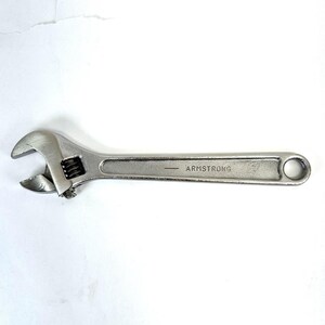 May include: A silver-colored metal adjustable wrench featuring a knurled adjustment screw and a smooth handle. The word ARMSTRONG is clearly stamped into the side of the handle, accompanied by a small horizontal line mark near the text.