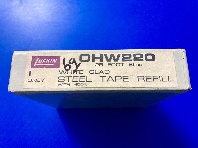 May include: A white box with black text that reads "OHW220 25 FOOT 8ths WHITE CLAD STEEL TAPE REFILL WITH HOOK ONLY". The box has a purple and white label that reads "LUFKIN".