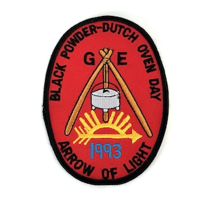 May include: Red patch with black border featuring text "BLACK POWDER-DUTCH OVEN DAY" and "ARROW OF LIGHT". The patch has a central design of a cooking pot suspended over a rising sun, with the year "1993" in blue.