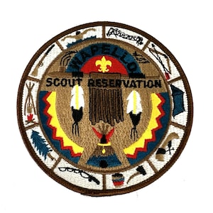 May include: A circular embroidered patch with the words "Wapello Scout Reservation" in a brown and blue design. The patch features Native American imagery, including feathers, a teepee, and a headdress, with a yellow fleur-de-lis.