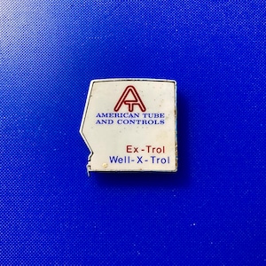May include: White metal tag with red lettering. The tag reads "American Tube and Controls" and "Ex-Trol Well-X-Trol". The tag has a large letter "A" with a smaller "T" inside of it.