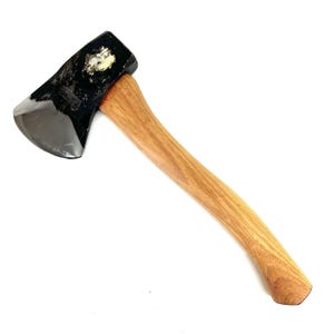 May include: A hand axe featuring a polished black metal head with a curved cutting edge and a light brown wooden handle. The metal head displays a metallic sheen and a distinct texture on the top surface, attached to a smooth, curved wooden grip.