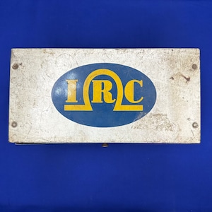 May include: A vintage metal box with a blue and yellow logo that says "IRC". The box is slightly worn and has a silver finish.