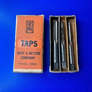 May include: A set of three metal taps in a cardboard box. The box is labeled "TAPS" and "REIFF & NESTOR COMPANY, LYKENS, PENNA."