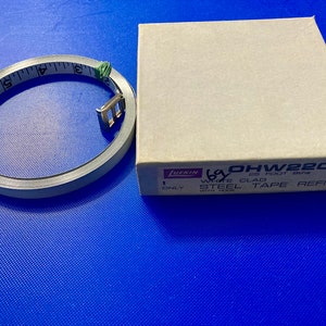 May include: A Lufkin 25 foot tape measure refill in a brown box. The box says "1 Only White Clad Steel Tape Refill with Hook" and the model number is "OHW220".