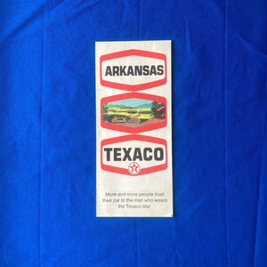May include: A vintage Texaco road map for the state of Arkansas. The map features a red and white Texaco star logo and the text "More and more people trust their car to the man who wears the Texaco star."