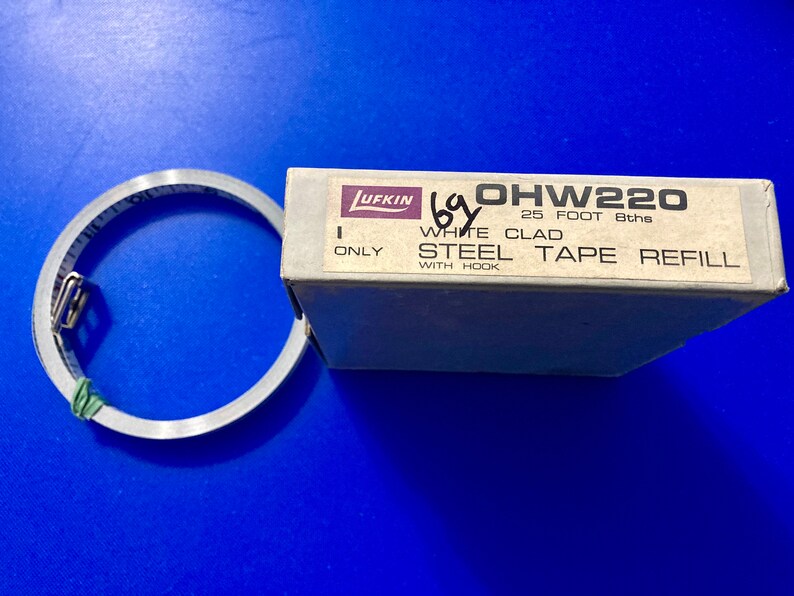 May include: A white box with the text "OHW220 25 FOOT 8ths WHITE CLAD STEEL TAPE REFILL WITH HOOK" and the Lufkin logo. A silver tape measure is next to the box.