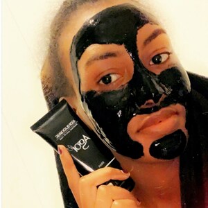 May include: A person is applying a black charcoal face mask. The mask is covering most of their face, leaving only their eyes and mouth visible. They are holding a black tube with the text "AOGA BLACK MASK" printed on it.