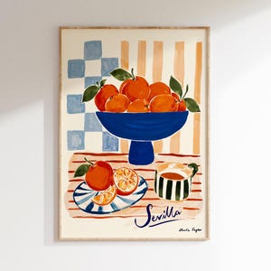 K&ouml;nnte beinhalten: Gerahmter Kunstdruck mit einem Stillleben aus Orangen in einer blauen Schale, einem gestreiften Teller mit Orangenscheiben und einer Tasse Tee. Das Wort "Sevilla" ist kursiv geschrieben. Der Hintergrund hat ein kariertes und gestreiftes Muster.