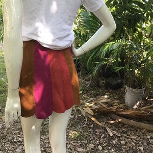 May include: A short skirt with a brown, pink and orange colour block design. The skirt is made of a suede-like material.