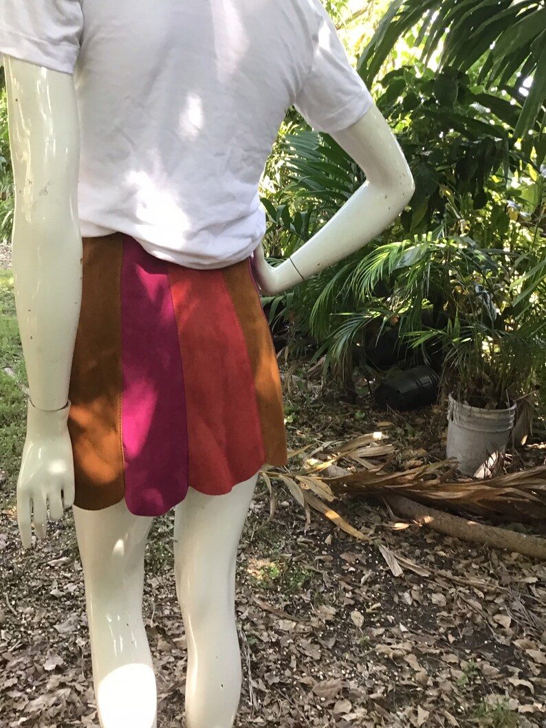 May include: A short skirt with a brown, pink and orange colour block design. The skirt is made of a suede-like material.
