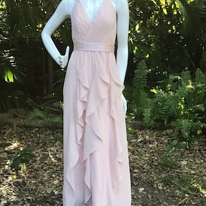 Puede incluir: Un vestido rosa claro de tirantes con falda de volantes y una faja de satén.