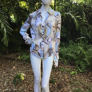 May include: A long-sleeved, light blue button-down shirt with a colorful print featuring chains, ribbons, and leopard spots.