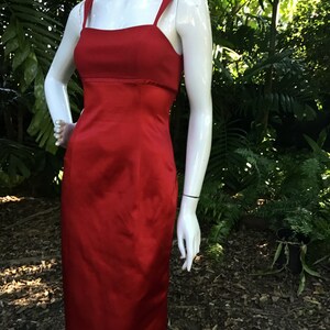 以下が含まれることがあります： フィットしたボディスとストレートスカートの赤いサテンのドレス。ドレスはスクエアネックラインと細いストラップです。
