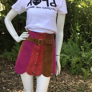 May include: A multi-coloured suede mini skirt with a scalloped hem. The skirt has a brown leather belt with a gold buckle and a row of gold buttons down the front.