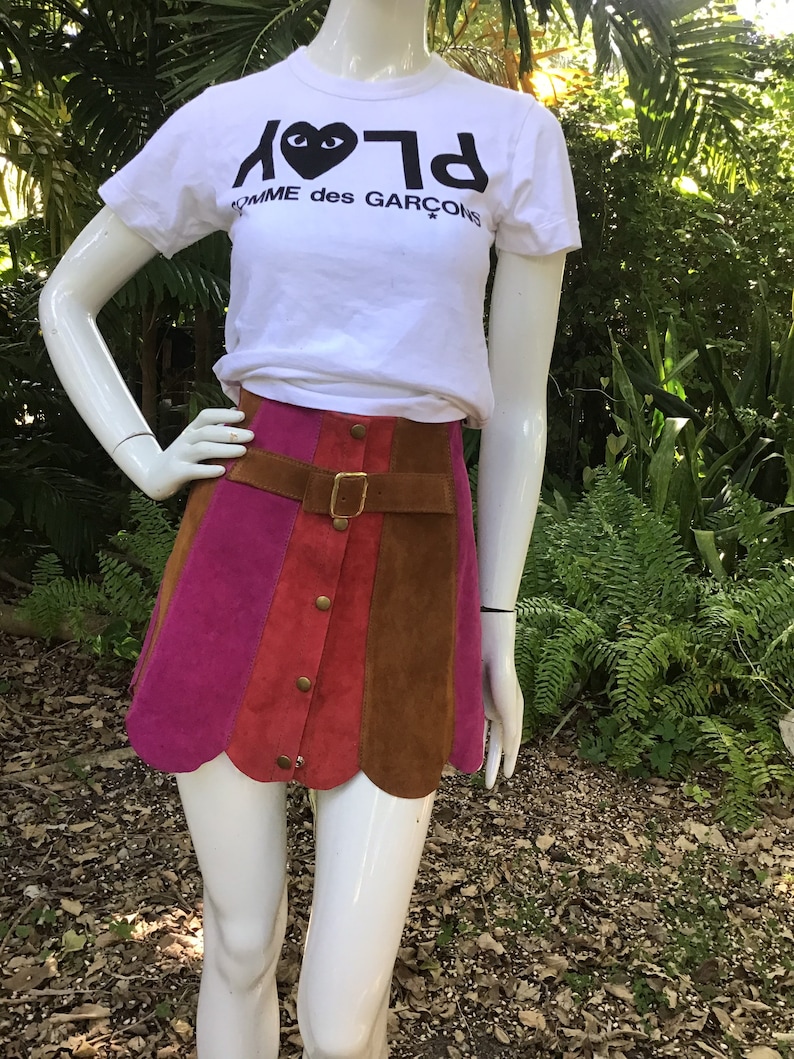 May include: A multi-coloured suede mini skirt with a scalloped hem. The skirt has a brown leather belt with a gold buckle and a row of gold buttons down the front.