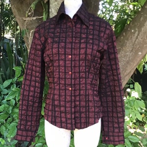 May include: A long-sleeved, burgundy button-down shirt with a black checkered pattern. The shirt has a slightly fitted silhouette and features red buttons.