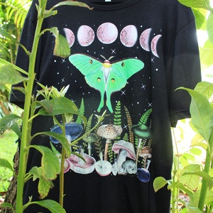 May include: Black t-shirt with a green luna moth, pink moon phases, and a variety of mushrooms printed on it.