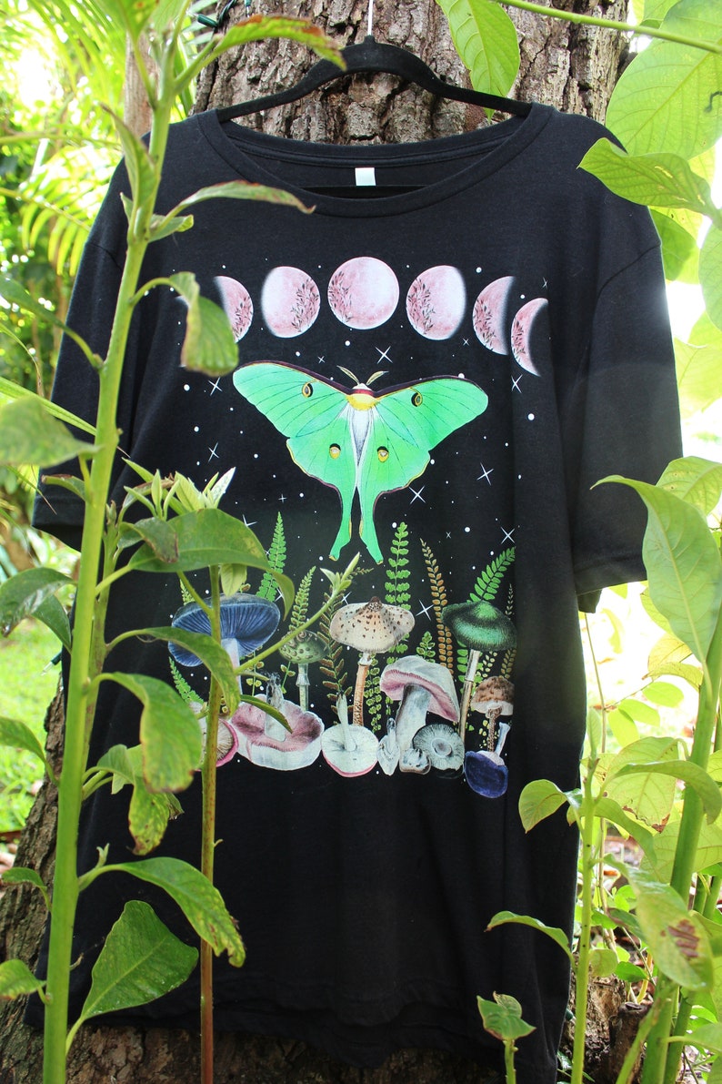 May include: Black t-shirt with a green luna moth, pink moon phases, and a variety of mushrooms printed on it.