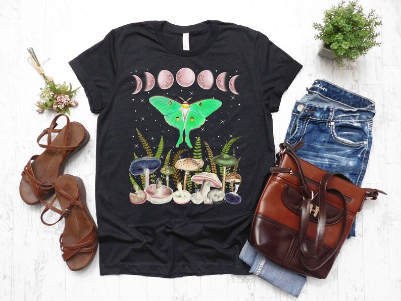 May include: Black t-shirt with a green luna moth, mushrooms, and a crescent moon design. The shirt has a relaxed fit and a crew neck.