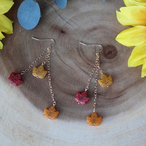 Op de afbeelding: Gouden oorhangers met drie herfstbladeren bedels in rood, oranje en geel.