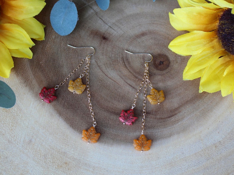 Op de afbeelding: Gouden oorhangers met drie herfstbladeren bedels in rood, oranje en geel.
