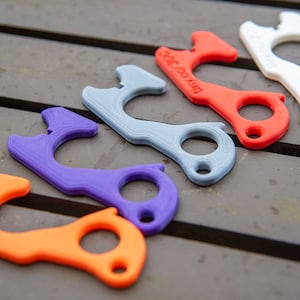 Könnte beinhalten: Fünf 3D-gedruckte Türöffner in verschiedenen Farben: orange, lila, grau, rot und weiß. Die Türöffner haben an einem Ende eine Schlaufe und am anderen Ende einen kleinen Haken.