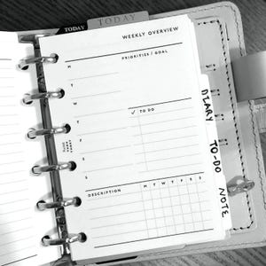 May include: A black and white weekly planner with tabs labelled "TODAY", "WEEKLY OVERVIEW", "DIARY", and "TO-DO NOTE". The planner has sections for priorities, goals, to-do list, and a daily schedule.