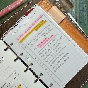 May include: A planner open to a page with handwritten notes and highlighted sections. The page is marked "Today 4/13" with a list of appointments. A pink pen is in the upper left corner, and the planner has a brown leather cover. The measurements are in cm.