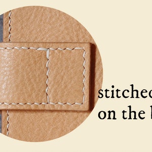 May include: Close-up of a tan leather strap with white stitching. The strap is stitched on the back.
